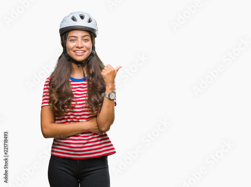 Young arab cyclist woman wearing safety helmet over isolated background smiling with happy face looking and pointing to the side with thumb up.