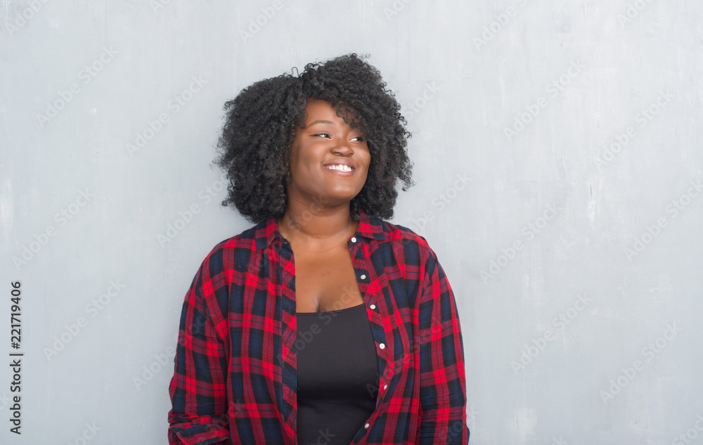 Young african american hipster woman over grey grunge wall looking away to side with smile on face, natural expression. Laughing confident. Young african american hipster woman over grey grunge wall looking away to side with smile on face, natural expression. Laughing confident.