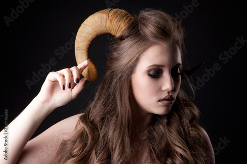 Portrait of an attractive demon woman with horns and curly hair, studio shot for Halloween