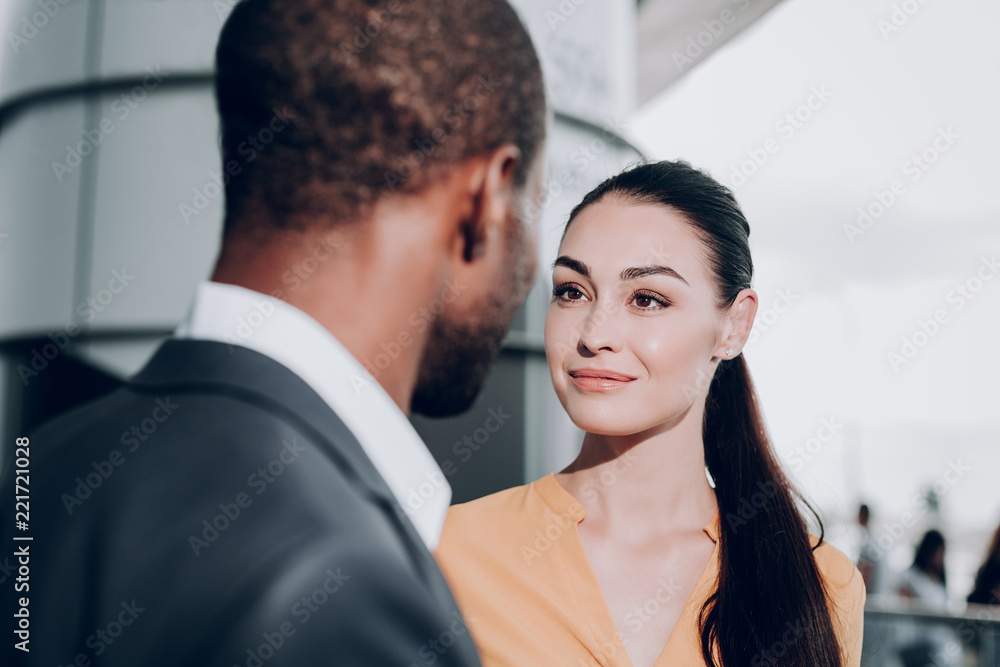 Pleasant meeting. Close up portrait of two people meeting each other. Focus on graceful girl in yellow shirt looking candidly at male who stands back to the camera Pleasant meeting. Close up portrait of two people meeting each other. Focus on graceful girl in yellow shirt looking candidly at male who stands back to the camera