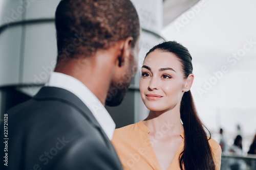 Pleasant meeting. Close up portrait of two people meeting each other. Focus on graceful girl in yellow shirt looking candidly at male who stands back to the camera photo