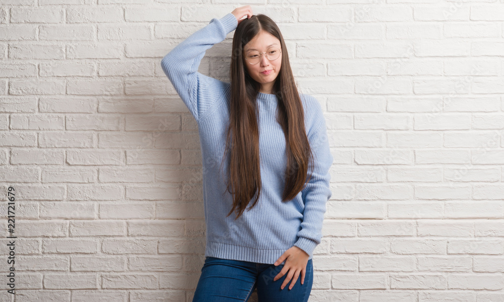 Young Chinise woman over white brick wall confuse and wonder about question. Uncertain with doubt, thinking with hand on head. Pensive concept. Young Chinise woman over white brick wall confuse and wonder about question. Uncertain with doubt, thinking with hand on head. Pensive concept.