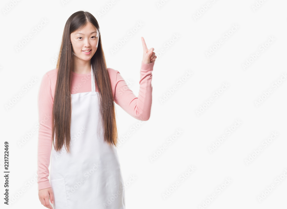 Young Chinese shop owner woman over isolated background wearing white apron surprised with an idea or question pointing finger with happy face, number one Young Chinese shop owner woman over isolated background wearing white apron surprised with an idea or question pointing finger with happy face, number one