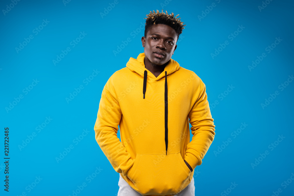 My favorite sweatshirt. .Waist up portrait of young man in yellow hoodie  hiding hands in pockets. He is looking at camera with serious expression  Photos | Adobe Stock