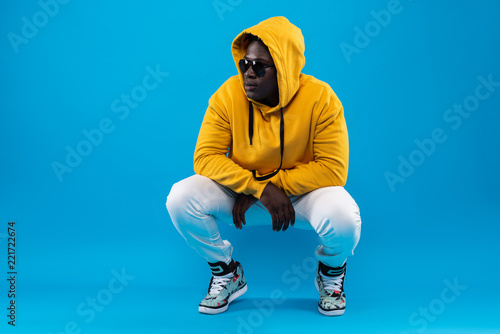 My style. Studio portrait of young man in yellow hoodie hunkering