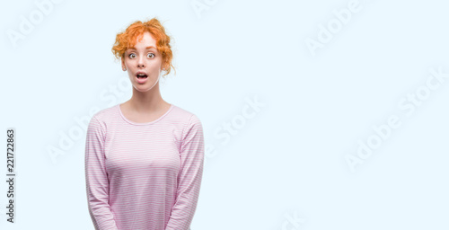 Young redhead woman afraid and shocked with surprise expression, fear and excited face.