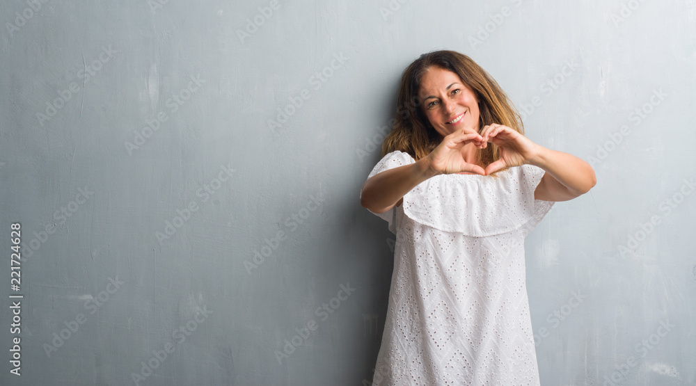 Middle age hispanic woman standing over grey grunge wall smiling in love showing heart symbol and shape with hands. Romantic concept. Middle age hispanic woman standing over grey grunge wall smiling in love showing heart symbol and shape with hands. Romantic concept.