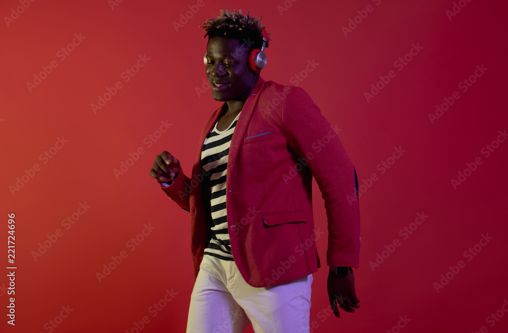 Having fun. Portrait of smiling guy in headphones is listening favorite song and moving to the rhythm. Isolated on red background
