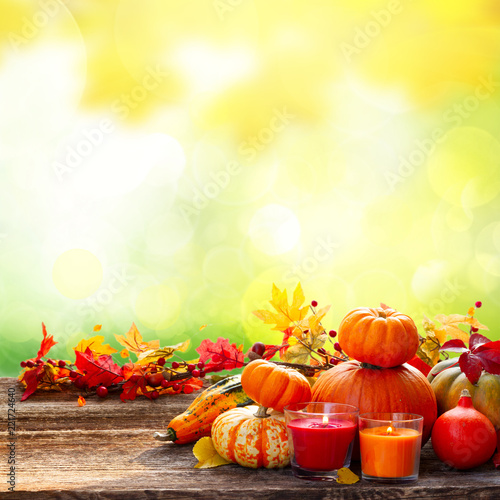 Fall harvest of raw pumpkins with leaves and candles on wooden table border over garden background