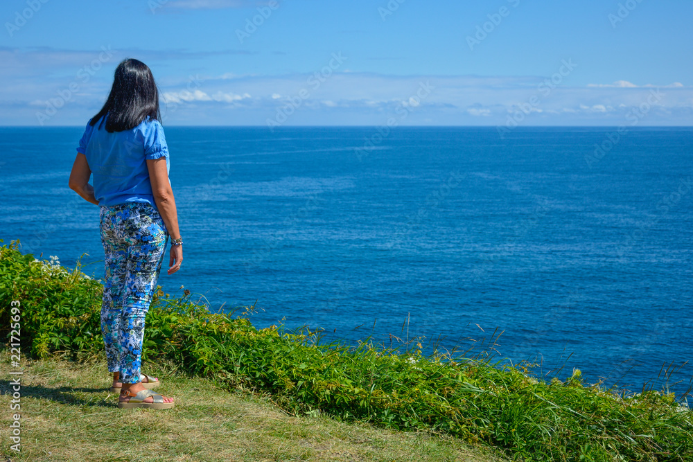 Mujer morena vestida de azul mirando al mar Cantábrico, verano, Santander, España