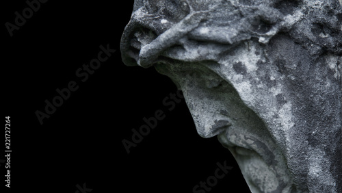 An ancient statue of the crucifixion of Jesus Christ in profile against black background