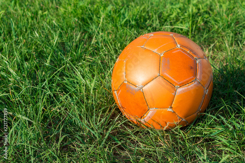 Orange soccer ball on green grass. The concept of street football. An old ball with cracks. Healthy lifestyle. Sport. Victory.