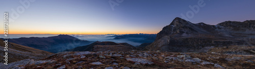 Colorful sunlight behind majestic mountain peaks of the Italian - French Alps, viewed from distant. Fog and mist covering the valleys below, autumnal landscape, cold feeling. © fabio lamanna