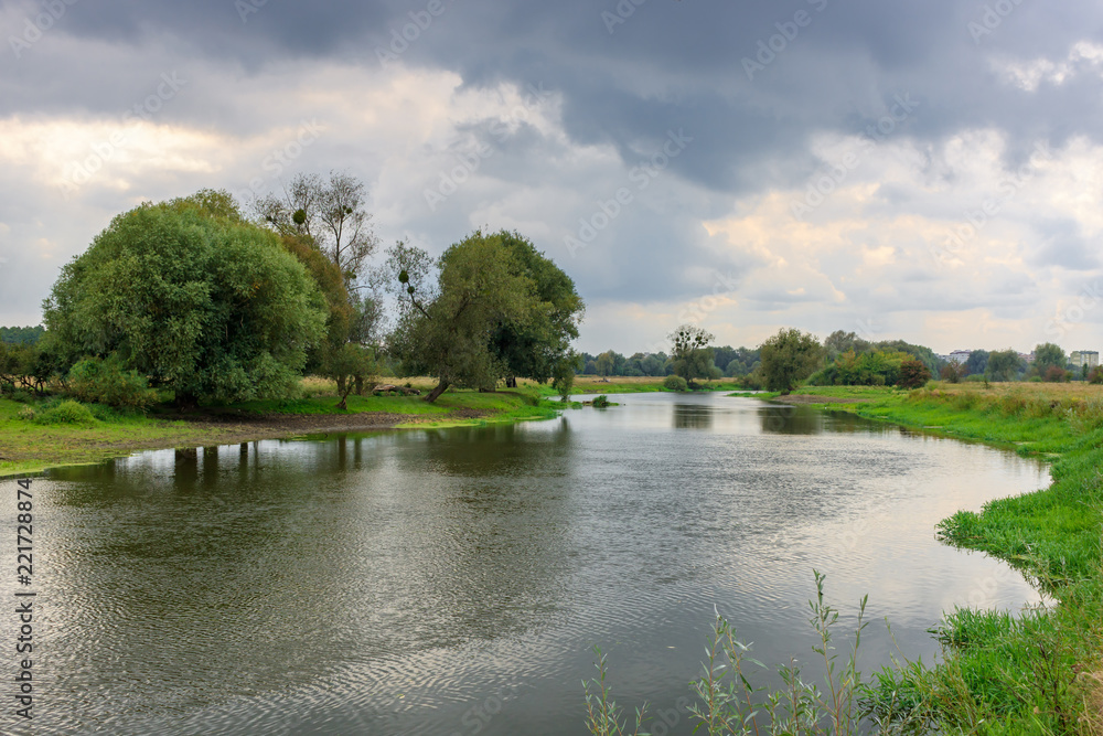 River landscape at cloudy autumn day against dramatic sky with gray clouds