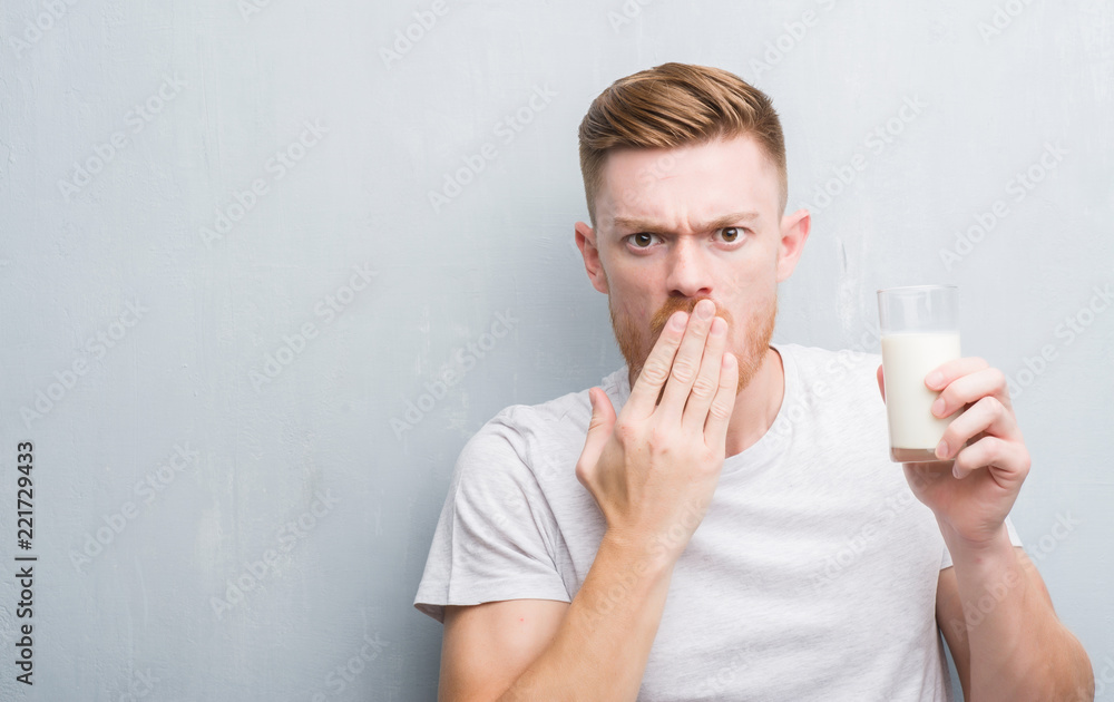 Young redhead man over grey grunge wall drinking a glass of milk cover mouth with hand shocked with shame for mistake, expression of fear, scared in silence, secret concept Young redhead man over grey grunge wall drinking a glass of milk cover mouth with hand shocked with shame for mistake, expression of fear, scared in silence, secret concept