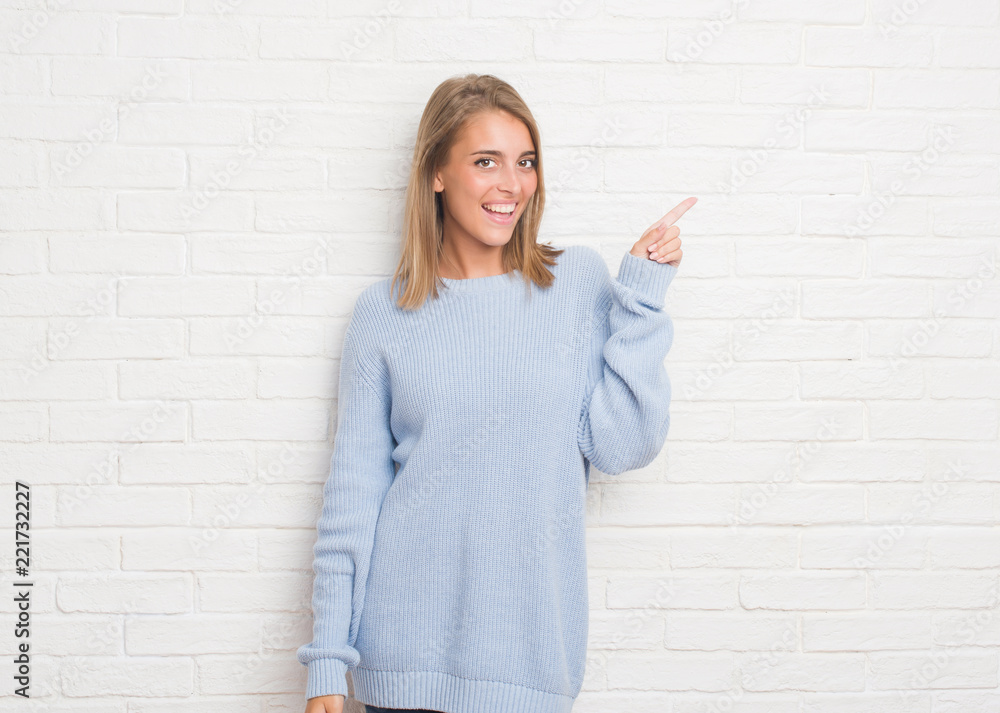 Beautiful young woman over white brick wall with a big smile on face, pointing with hand and finger to the side looking at the camera. Beautiful young woman over white brick wall with a big smile on face, pointing with hand and finger to the side looking at the camera.