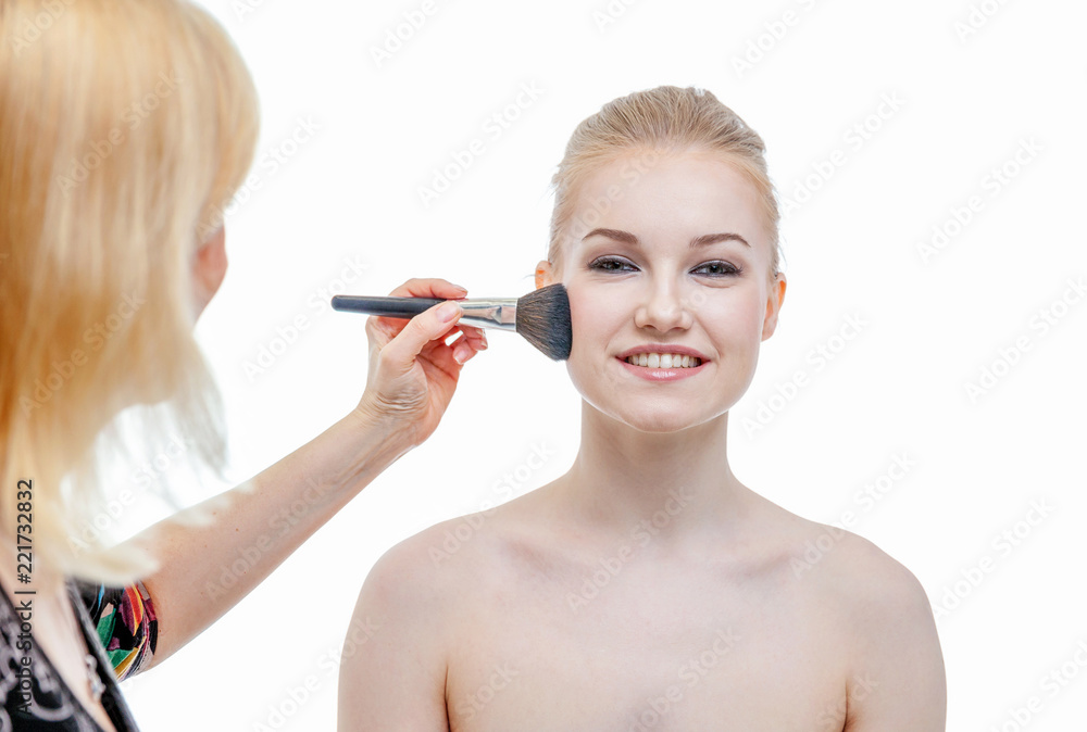 Fototapeta premium Hand of makeup master applying powder for young woman model on white background. Professional make up applying by artist. Beautiful girl face with perfect skin. Make-up detail in process