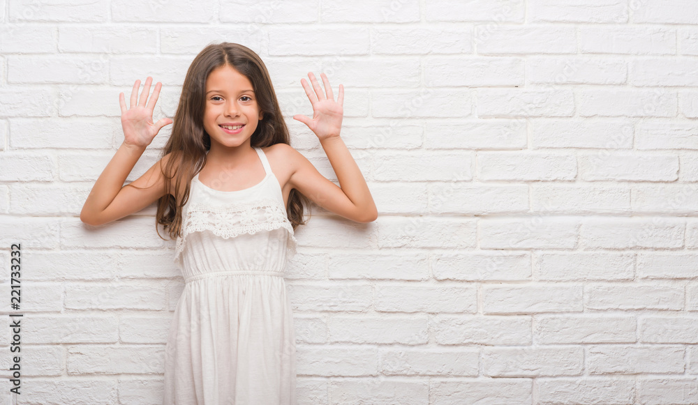 Young hispanic kid over white brick wall showing and pointing up with fingers number ten while smiling confident and happy.