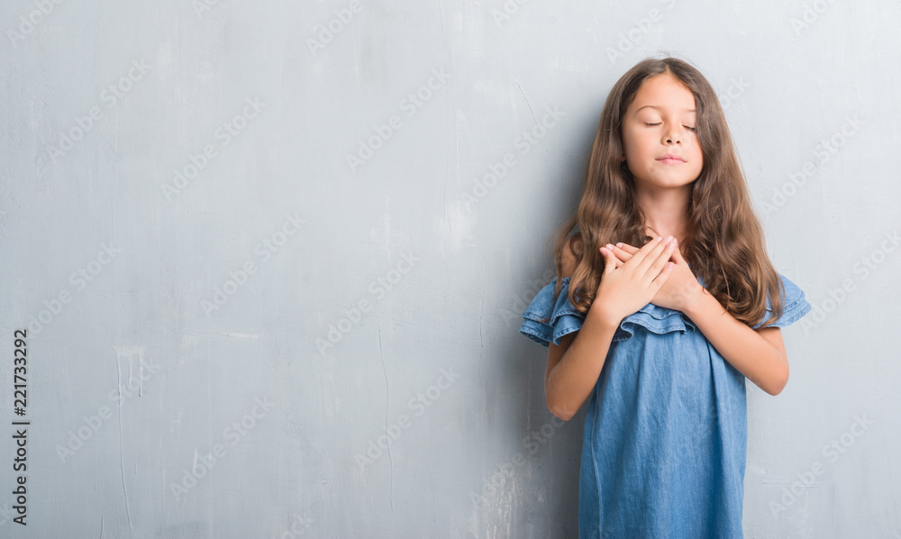 Young hispanic kid over grunge grey wall smiling with hands on chest with closed eyes and grateful gesture on face. Health concept. Young hispanic kid over grunge grey wall smiling with hands on chest with closed eyes and grateful gesture on face. Health concept.