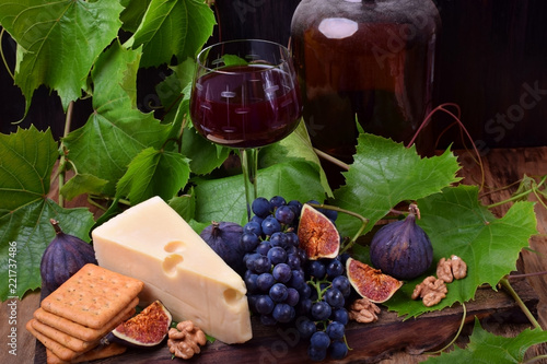 Red wine in a glass surrounded by the snacks: Maasdam cheese, figs, walnuts and a bunch of Isabella grapes on a wooden board