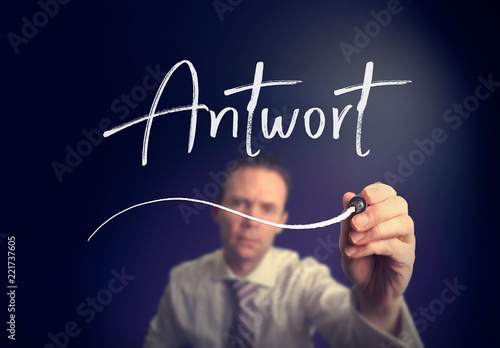 A businessman writing a Answer "Antwort" concept in German with a white pen on a clear screen.