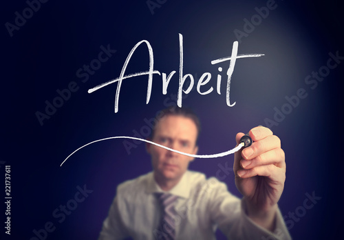 A businessman writing a Job "Arbeit" concept in German with a white pen on a clear screen.