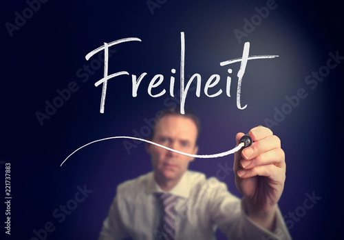 A businessman writing a Freedom "Freiheit" concept in German with a white pen on a clear screen.