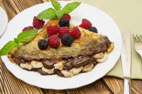 Homemade crepes served with chocolate cream, fresh blueberries and raspberries, powdered sugar on a white background