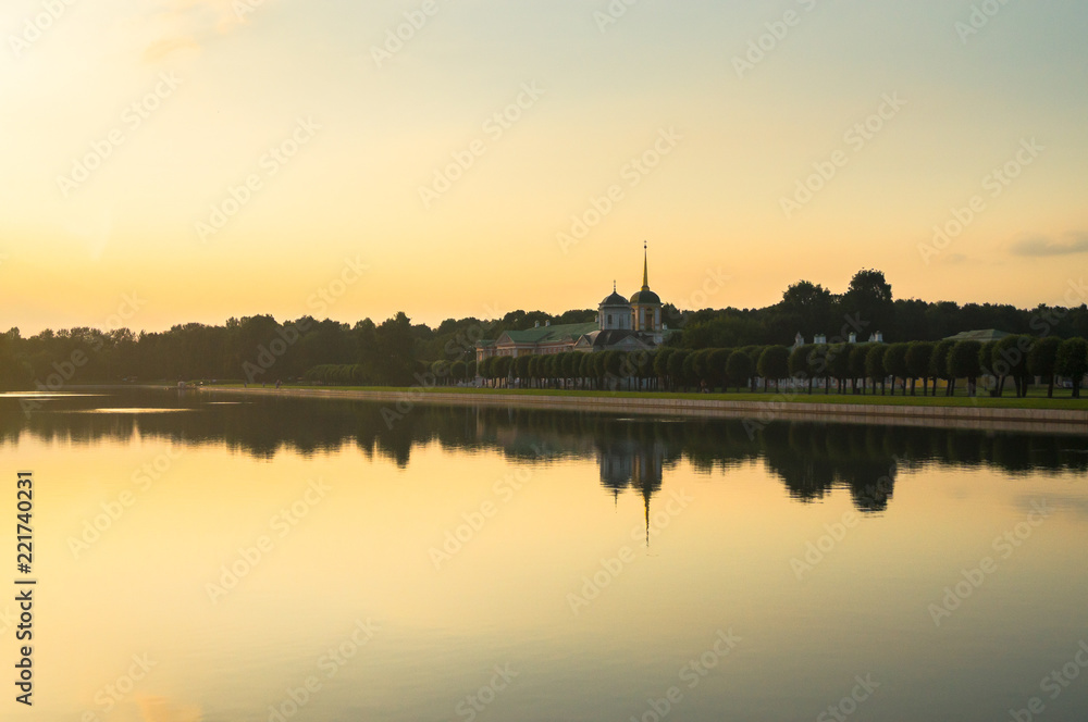 Golden sunset on the palace pond of the State reserve Kuskovo, Moscow. Russia. Mysterious moment when the orange sun says goodbye to nature. Its last reflection trembles on the water. 