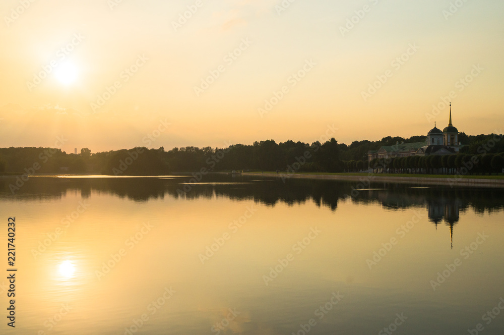 Golden sunset on the palace pond of the State reserve Kuskovo, Moscow. Russia. Mysterious moment when the orange sun says goodbye to nature. Its last reflection trembles on the water. 