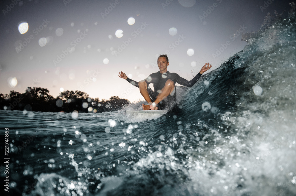 Happy wakesurfer sitting on the board on the background of focused blue splashing wave