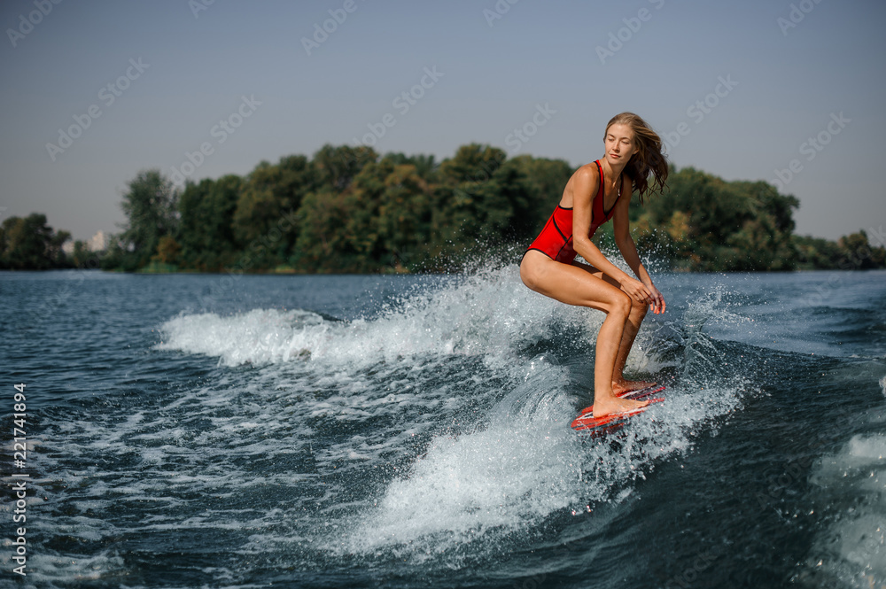 Young blonde woman wakesurfer riding down the blue splashing wave