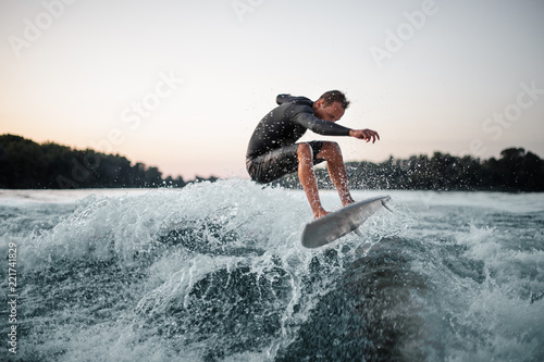 Professional wakeboarder jumping on the blue splashing wave against the background of clear sky on the foreground