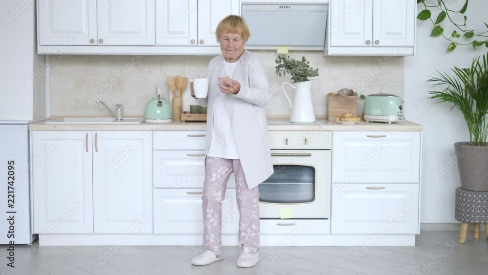 Cheerful Aged Woman Dancing In Kitchen With Smartphone Cheerful Aged Woman Dancing In Kitchen With Smartphone