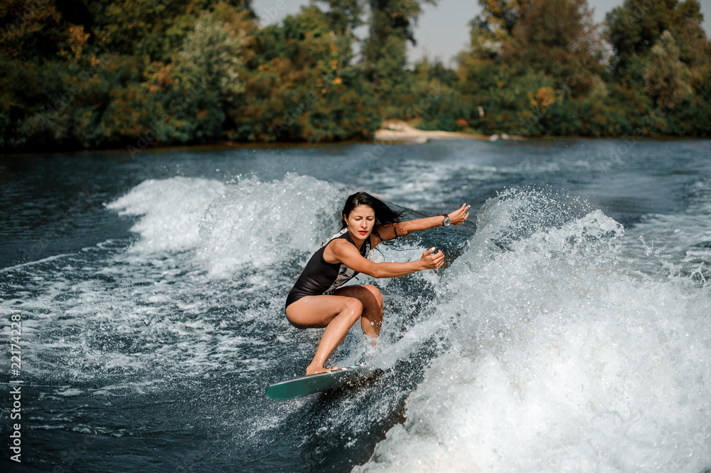 Fototapeta premium Brunette woman wakesurfing on board down the blue water