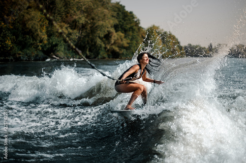 Sexy smiling brunette woman wakesurfing on board down the blue water