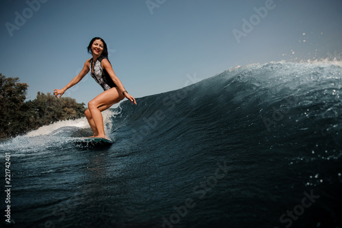 Happy brunette woman wakesurfing on board down the blue water