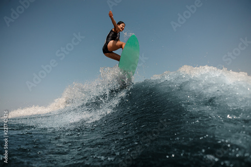 Sexy brunette woman jumping on a wakeboard on the high blue wave © fesenko