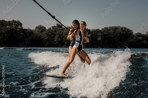 Two sexy women wakesurfing on one board down the blue water © fesenko