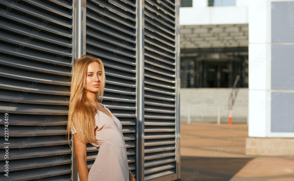 Fototapeta premium Attractive tanned model in fashionable outfit posing at the background of metal shutters. Space for text