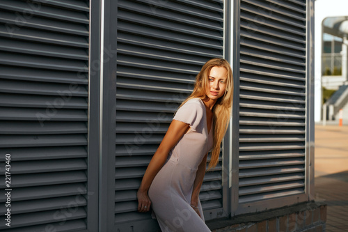Amazing tanned model in fashionable outfit posing at the background of metal shutters. Space for text