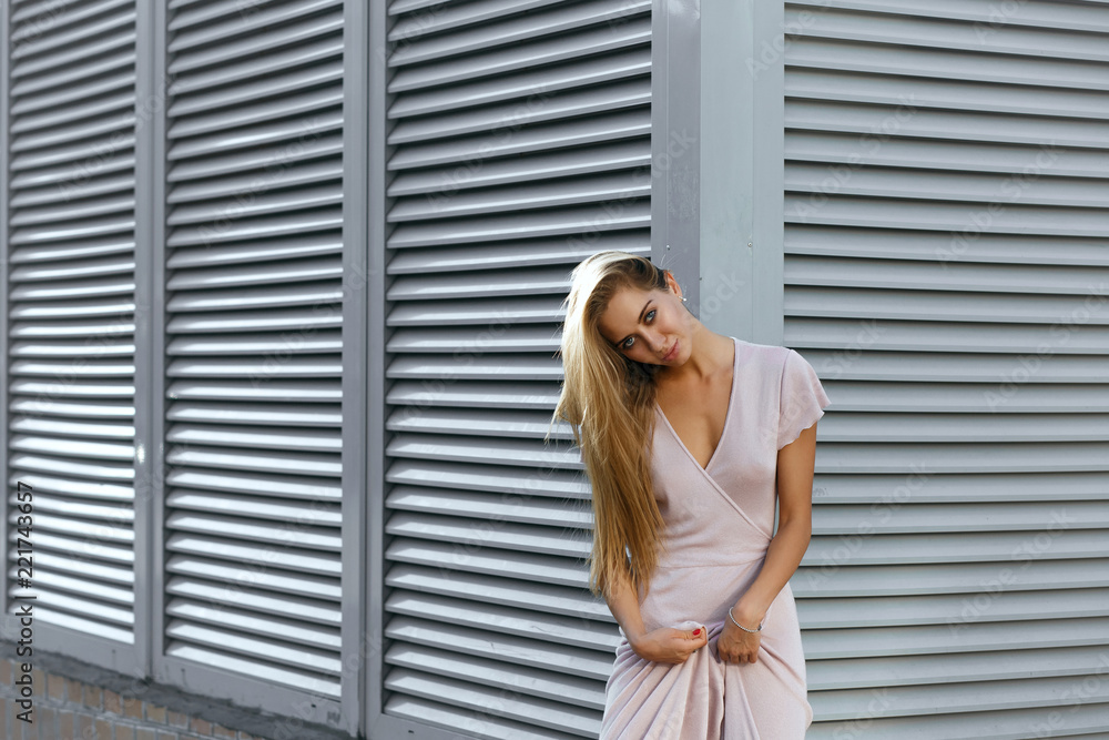 Sexy tanned model in fashionable outfit posing at the background of metal shutters. Space for text