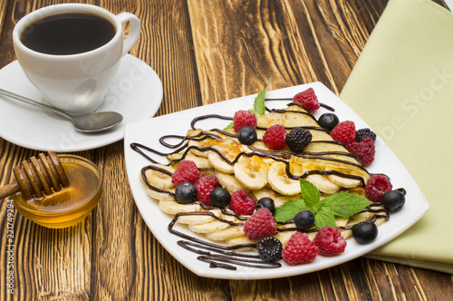 Homemade crepes served with chocolate cream, Banana, fresh blueberries, raspberries on a wooden background, pancakes