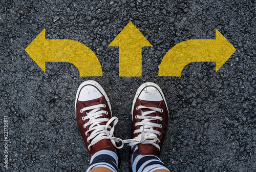 man legs in sneakers standing on road with three direction arrow choices, left, right or move forward