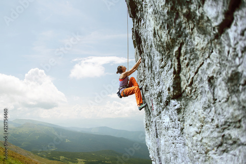 Fototapeta young slim female rock climber climbing on the cliff