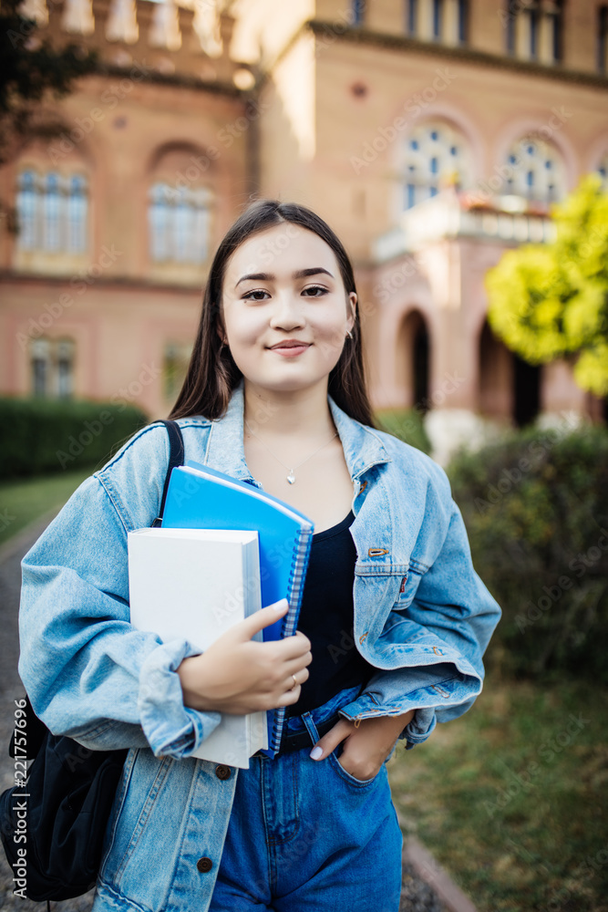 Fototapeta premium Happy young asian female student at college campus and carrying books