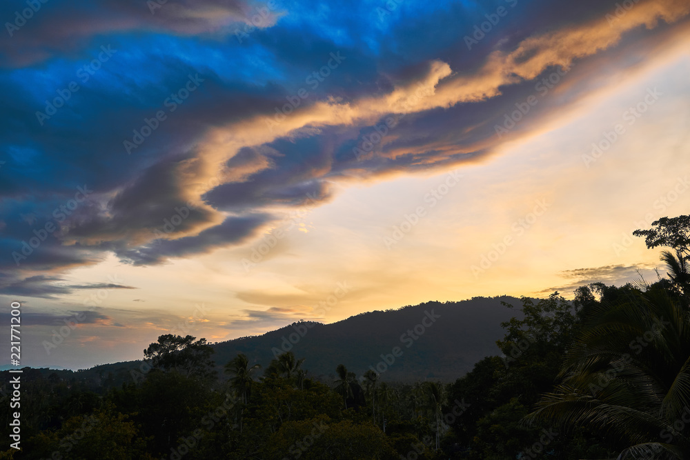 Dramatic clouds against the backdrop of mountains at sunset on a tropical island.
