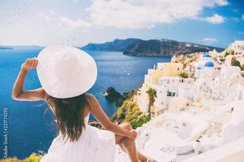 Tourist woman at view of Santorini cruise travel. Beautiful white village of Oia with Caldera and mediterranean sea. Girl in sun hat and red dress enjoying summer travel vacation in Europe.