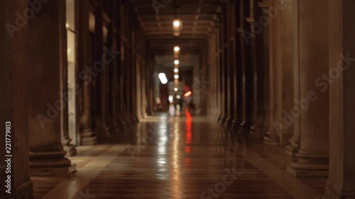 Hallway lined up with columns in the ancient building on St. Marks Square. Dim light, people walking in the distance photo