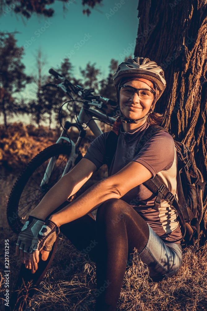 Naklejka premium Woman in helmet sitting at sunset near her bicycle